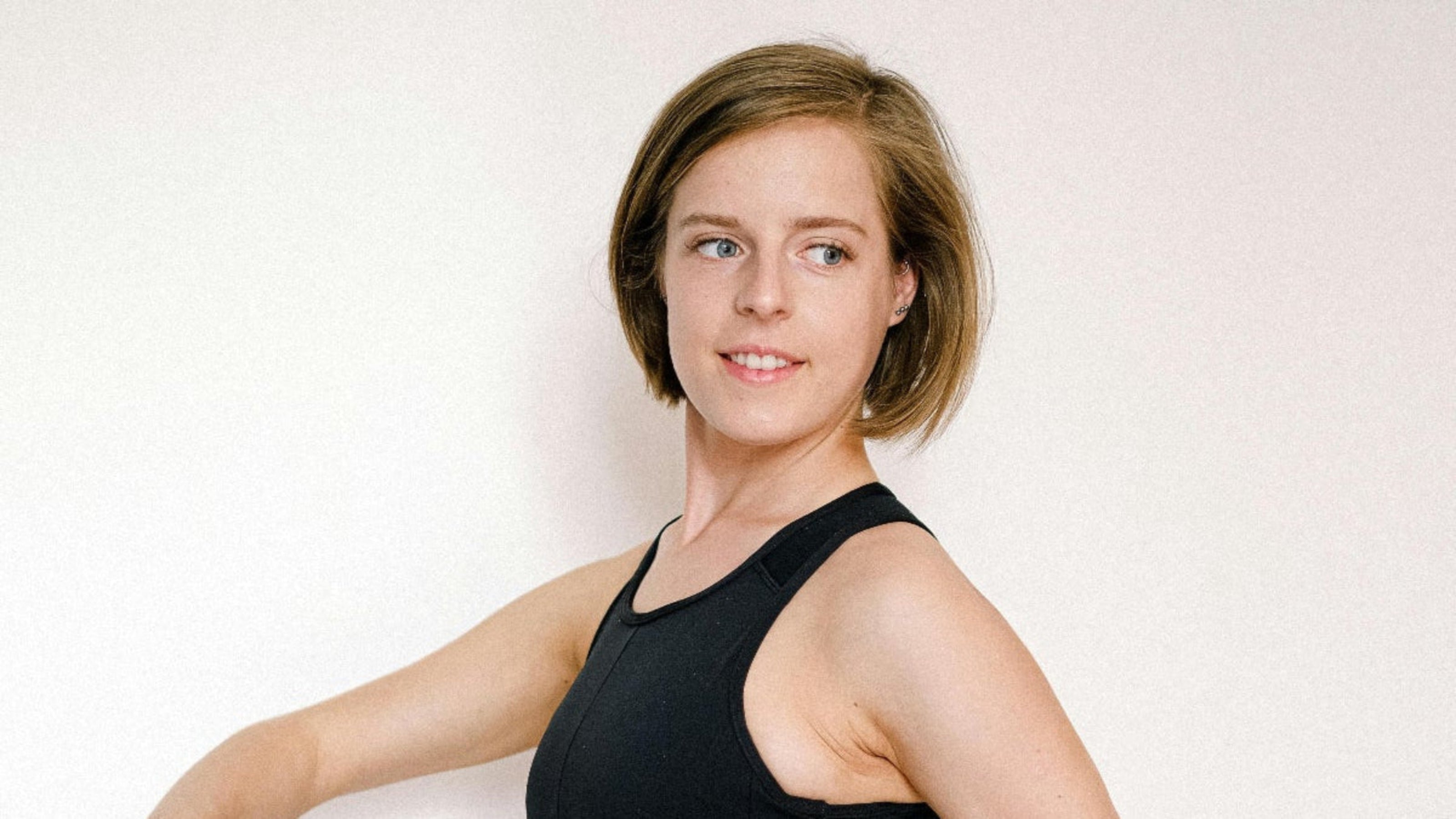 Woman wearing a black sports bra and beige leggings with black mesh panels on a white background